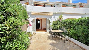 A courtyard with a stone floor, a round table with chairs, and a white building with a tiled roof. - Jane - modern, well-equipped bungalow in Moraira (Teulada)