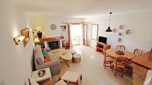A living room with a sofa, coffee table, and dining table with chairs. There is a fireplace, a television, and a mirror on the wall. - Jane - modern, well-equipped bungalow in Moraira (Teulada)