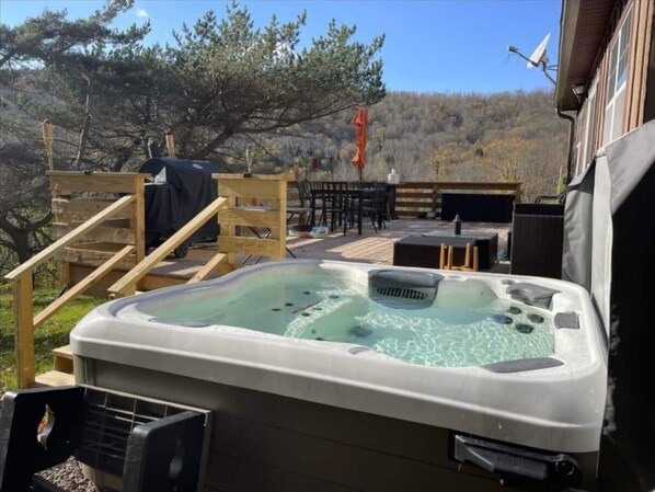 Relax in the hot tub on the deck, surrounded by a serene natural landscape.