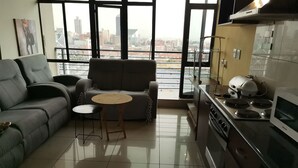 Una sala de estar moderna con un sofá gris, una mesita redonda y una cocina con estufa y microondas.