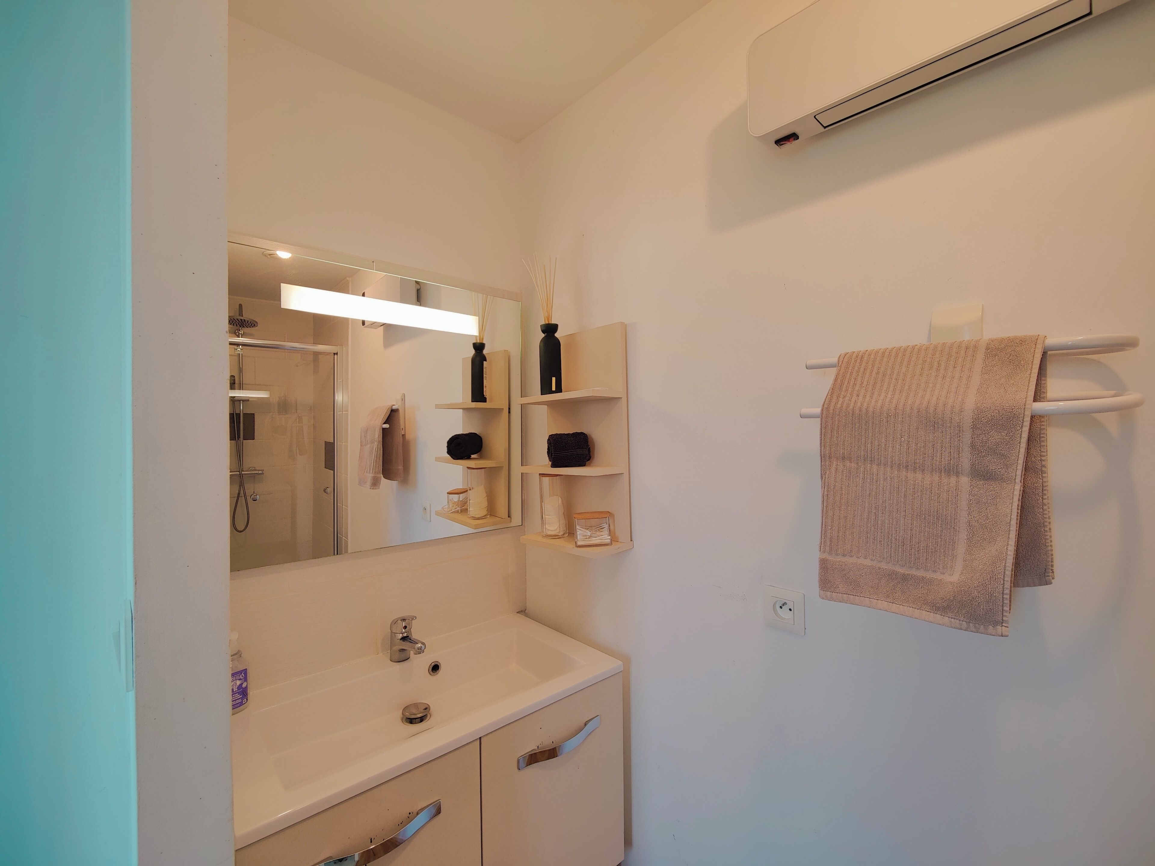 A bathroom with a mirror, a sink, a towel rack, and a shower.