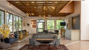 A modern interior with a wooden ceiling, large windows, a sofa, chairs, a rug, and a kitchen area.