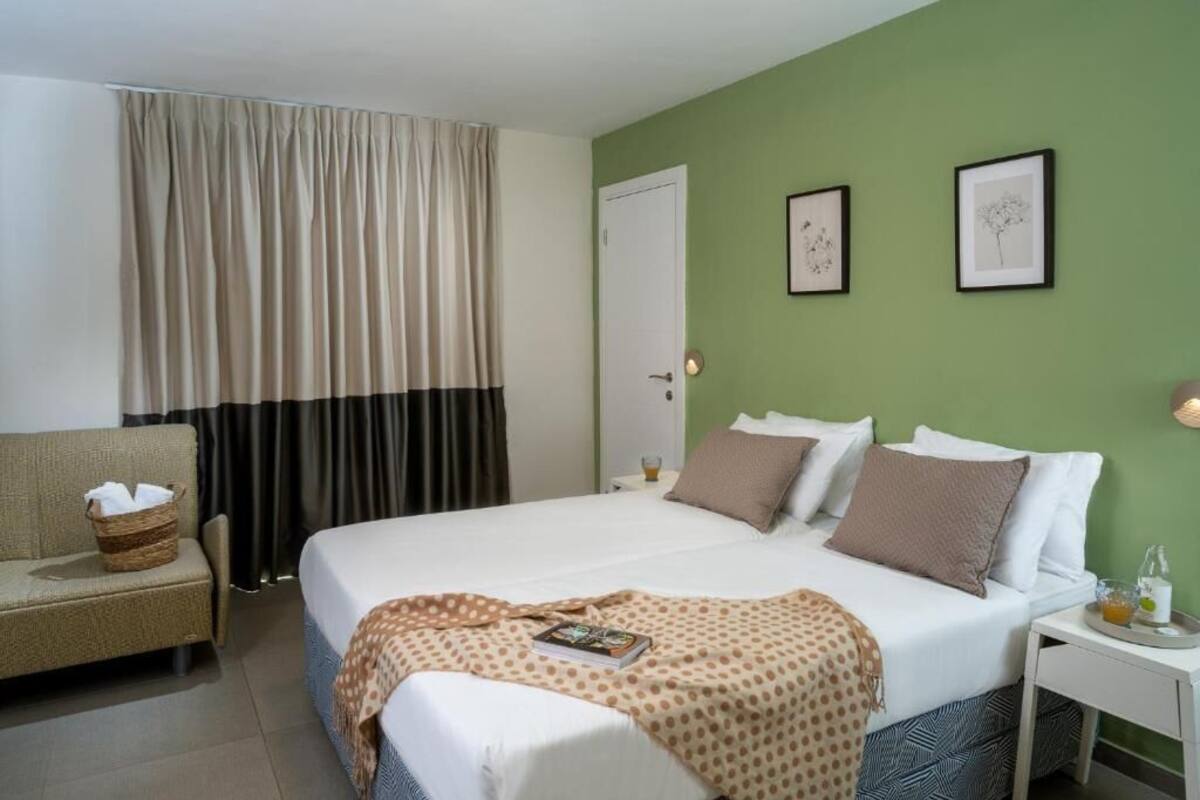 Habitación de hotel con cama, una silla, una mesita de noche y ventana con cortinas.