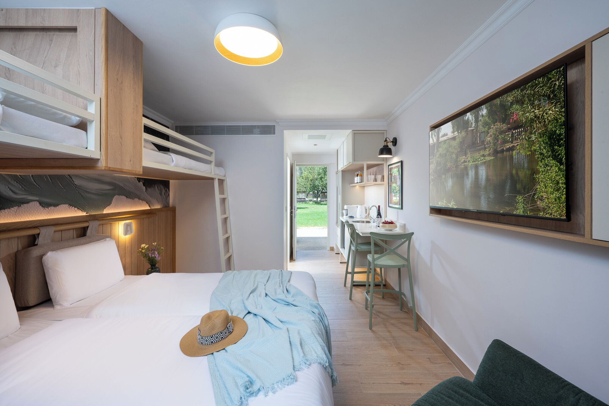 A bedroom with a bunk bed, a desk, and a view of a garden.