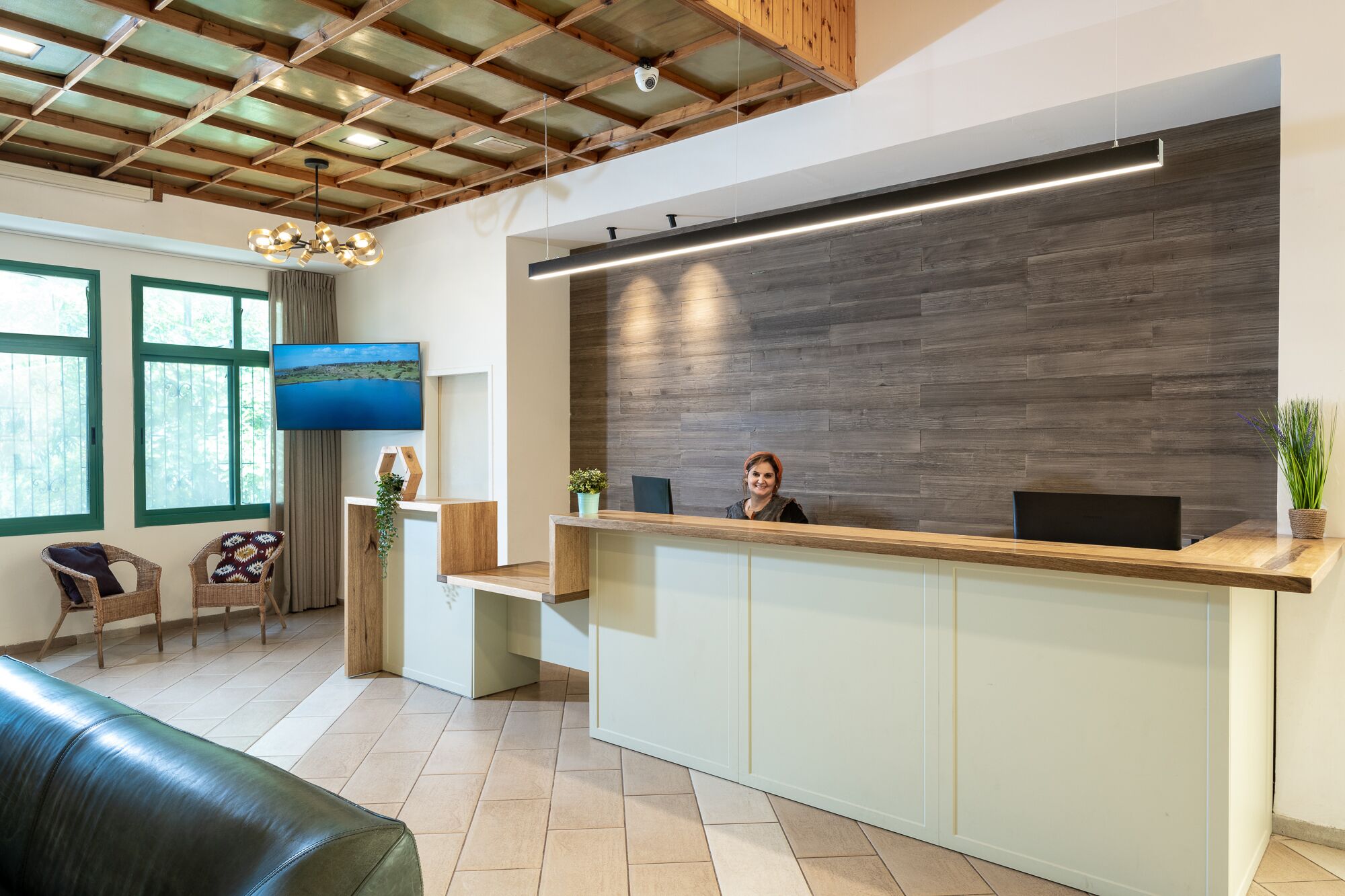 A reception area with a wooden reception desk, a flat-screen TV mounted on the wall, and a large window with a view of greenery.