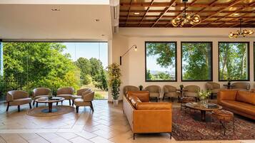 A spacious living area with a large window, a ceiling with wooden beams, and a modern chandelier.