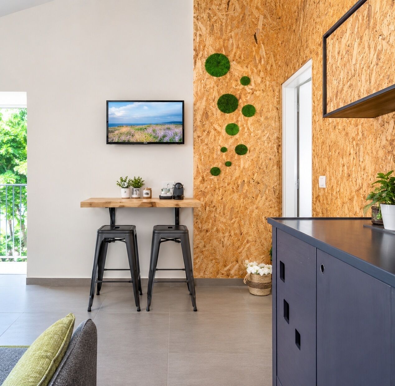 Una cocina moderna con un revestimiento de madera, un televisor de pantalla plana, una mesa de madera con taburetes y un mueble de color oscuro.