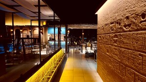 An outdoor dining area with tables and chairs, a pool, and a stone wall with carvings. - Historia Royal (Udaipur)