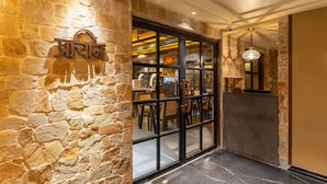 A stone wall with a sign, a glass door leading to a dining area, and a hanging light fixture. - Historia Royal (Udaipur)