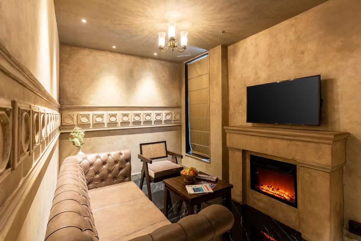 A cozy living room with a fireplace, a flat-screen TV, a sofa, and a small table with a vase and magazines.