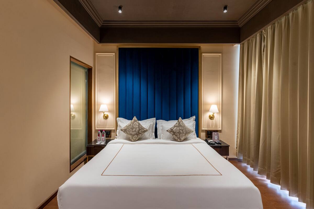 A hotel room with a large bed, two bedside tables, a mirror, and a blue headboard.