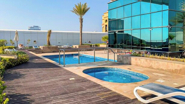 A rooftop pool area with two pools, lounge chairs, and a modern building with glass windows. - Gld - Cozy Studio with balcony (Dubai)