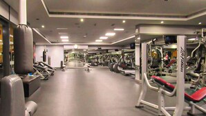 A gym with various exercise machines, a large punching bag, and a mirrored wall. - Gld - Cozy Studio with balcony (Dubai)