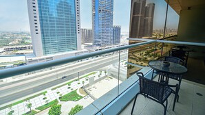 A balcony with a view of a cityscape, including tall buildings and a road. There is a table and two chairs on the balcony. - Gld - Cozy Studio with balcony (Dubai)