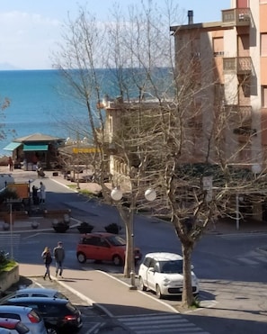 Une rue bordée de voitures garées, un arbre et des bâtiments en arrière-plan.