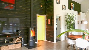 A modern living room with a fireplace, wooden flooring, a dining area with a table and chairs, and a large green plant.