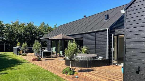 A modern house with a wooden deck, outdoor seating, and a hot tub.