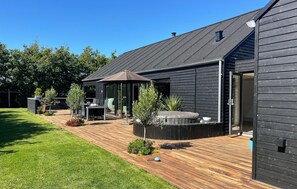 A modern house with a wooden deck, outdoor seating, and a hot tub.