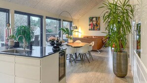 A modern kitchen with a central island, large windows, and a dining area with a brown leather couch.