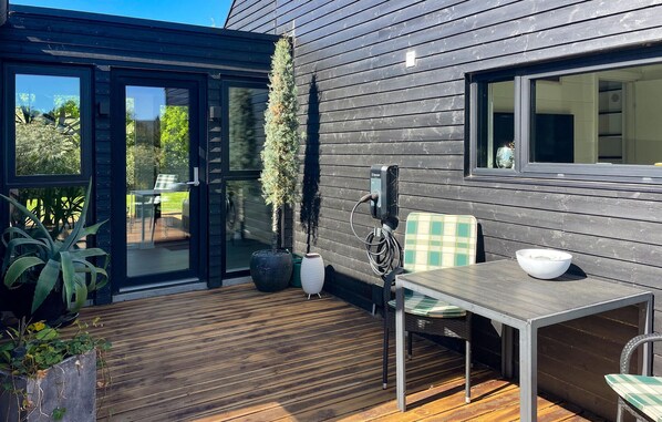A modern outdoor patio with a wooden deck, a table with chairs, and a solar panel charging station.