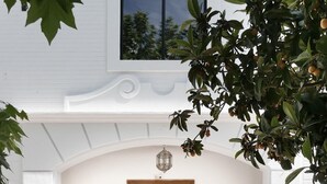 A white building with a wooden double door, a small window above the door, and a decorative balcony railing. - Orchard of the Purisima (Santa Fe)