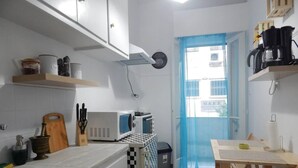 Een kleine keuken met witte kastjes, een magnetron, een koffiezetapparaat en een geruite vloer.
