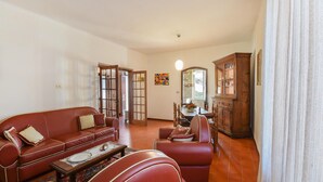 A living room with a red sofa, a wooden cabinet, and a dining area with a table and chairs. - Nice home in Santo Stefano Magra with WiFi (Santo Stefano Magra)