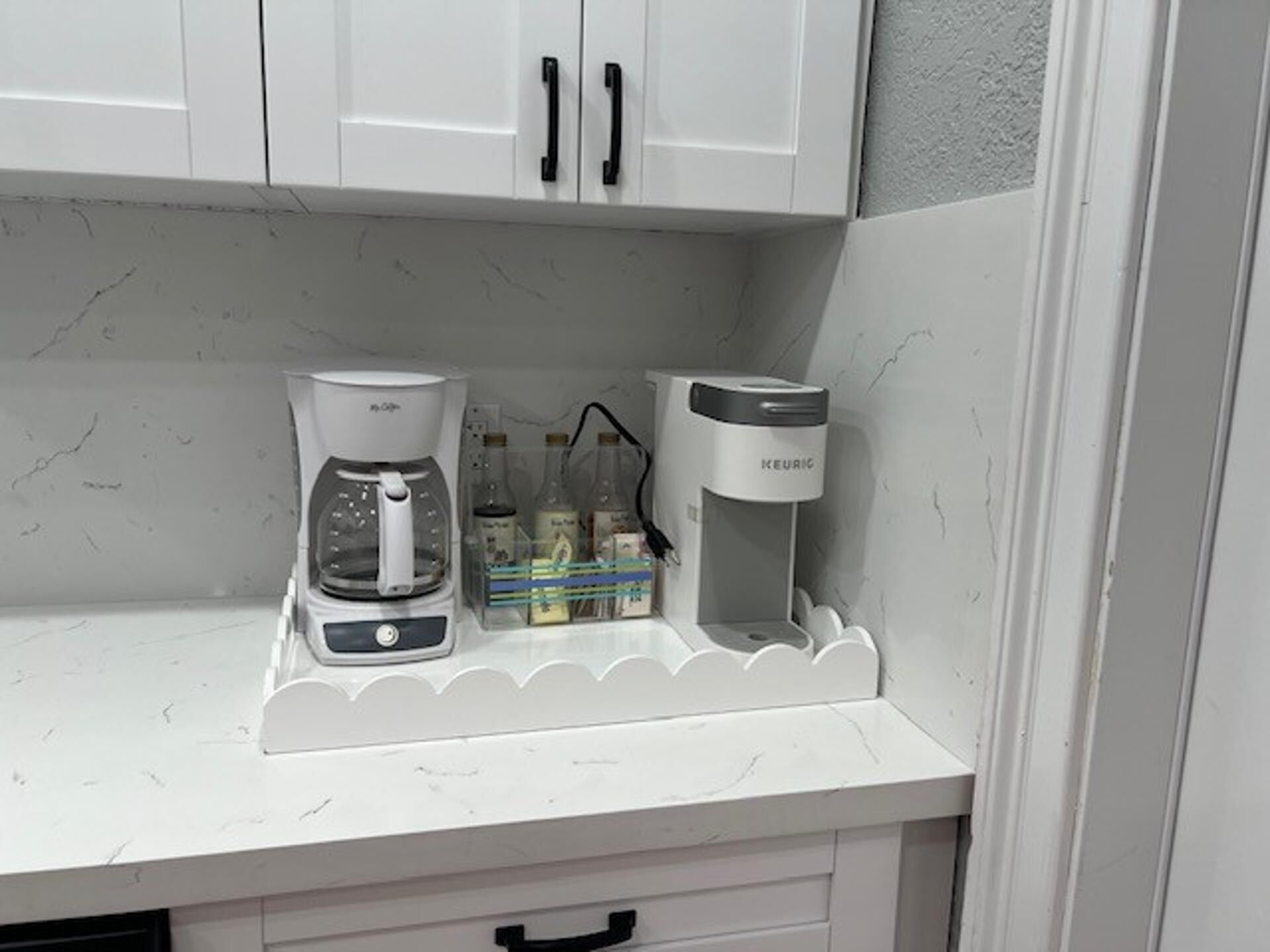 A kitchen with white cabinets, a coffee maker, and a water dispenser on a white countertop.