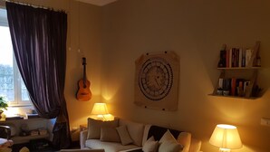 A cozy living room with a sofa, a coffee table, a guitar, a wall clock, and a bookshelf. - TRASTEVERE BOUTIQUE (Roma)