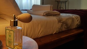 A neatly made bed with a white comforter and pillows, a wooden bedside table with a bottle of perfume, and a window with sheer curtains. - TRASTEVERE BOUTIQUE (Roma)