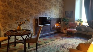 A living room with a TV, a fireplace, a dining table, and a patterned rug. - TRASTEVERE BOUTIQUE (Roma)