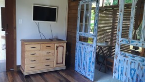 A wooden cabinet with drawers, a television mounted on the wall, and a rustic door with a distressed finish. - Ibiraquera Lagoon Studio (Imbituba)
