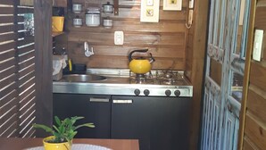 Een kleine keuken met houten wanden, een eettafel met stoelen, een gele pot op tafel en een fornuis.