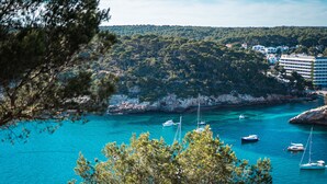 A coastal town with clear turquoise waters, boats, and a forested hill in the background. - Plaça de sa Punta, 4, 07750 Cala Galdana, Balearic Islands, Spanyolország (Cala Galdana)