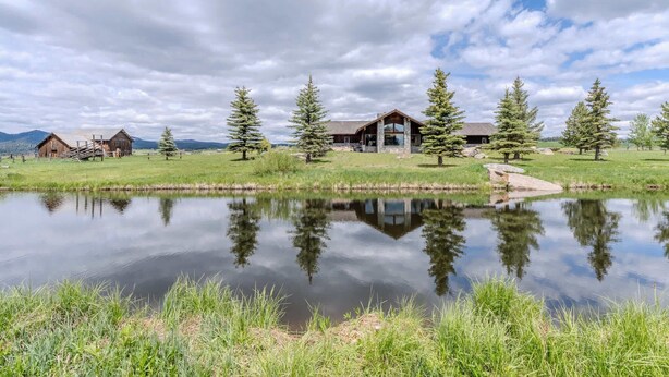 A lakeside property with a wooden cabin, a stone building, and a reflection in the water. - Otter Lodge (West Yellowstone)