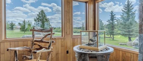 Una habitación con paredes de paneles de madera, una silla de madera, una mesa de piedra y un acuario con vista a un bosque.