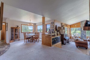 A spacious living area with a dining table, chairs, a fireplace, and a large window offering a view of the outdoors. - Otter Lodge (West Yellowstone)