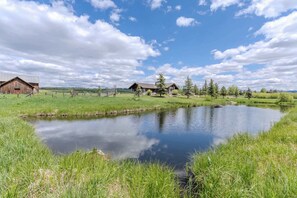 Ländliche Landschaft mit Teich, einem Holzstall und einem Haus mit Schrägdach.
