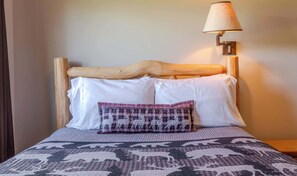 A bed with a wooden headboard, white pillows, a patterned blanket, and a lamp on a bedside table. - Otter Lodge (West Yellowstone)