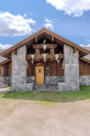 A lodge with a stone facade, wooden beams, and antlers displayed above the entrance. - Otter Lodge (West Yellowstone)