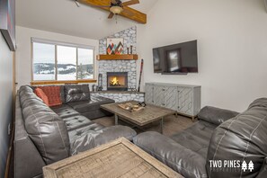 A modern living room with a stone fireplace, leather sofas, and a large window overlooking a snowy landscape.