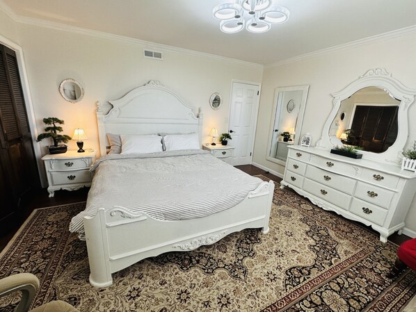 A bedroom with a large bed, a dresser, a nightstand, and a mirror.