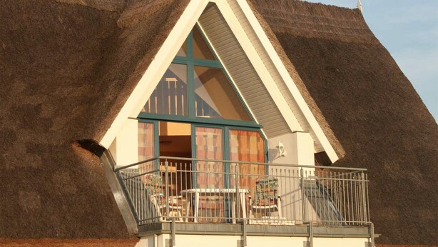 A thatched-roof building with a balcony and a window with curtains. - Cozy apartment in Börgerende-Rethwisch (Börgerende-Rethwisch)