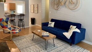A living room with a blue sofa, a wooden coffee table, a colorful armchair, a patterned rug, and a wall-mounted bicycle.
