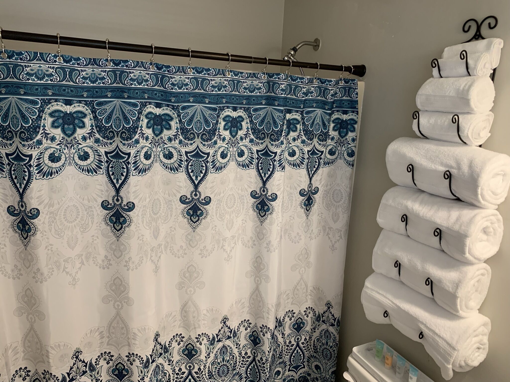 Un baño con cortina de ducha estampada, un perchero con toallas dobladas y un dispensador de papel higiénico.