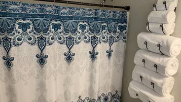 Un baño con cortina de ducha estampada, un perchero con toallas dobladas y un dispensador de papel higiénico.