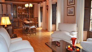 Un soggiorno con pavimento in legno, divani bianchi, una zona pranzo con tavolo e sedie e un vaso rosso su un tavolino.