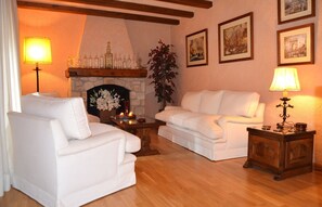 A living room with two white sofas, a fireplace, and framed pictures on the wall.