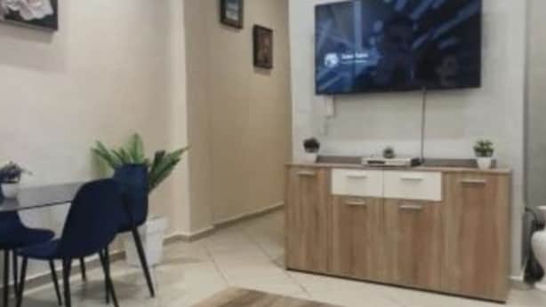 Una sala de estar moderna con una mesa de centro de madera, un televisor montado en la pared y un comedor con sillas y una mesa.