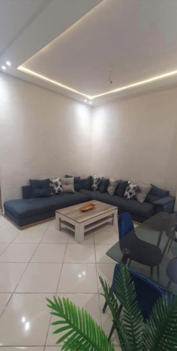 A modern living room with a dark blue sectional sofa, a wooden coffee table, and a glass dining table with chairs.